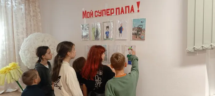 На снимке дети рассматривают рисунки, рассказывают о своих папах.