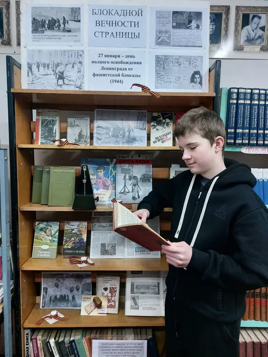 На фотографии читатель знакомится с документальной и художественной литературой, отображающая хронику блокадного Ленинграда