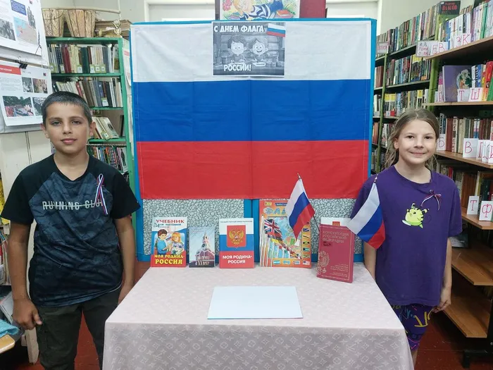 На фотографии у книжной выставки , посвящённой Дню флага России